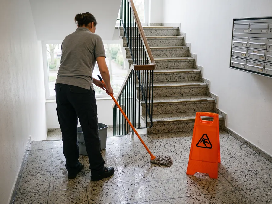 Treppenhausreinigung in einem Mehrfamilienhaus in Köln: Reinigungskraft wischt das Podest